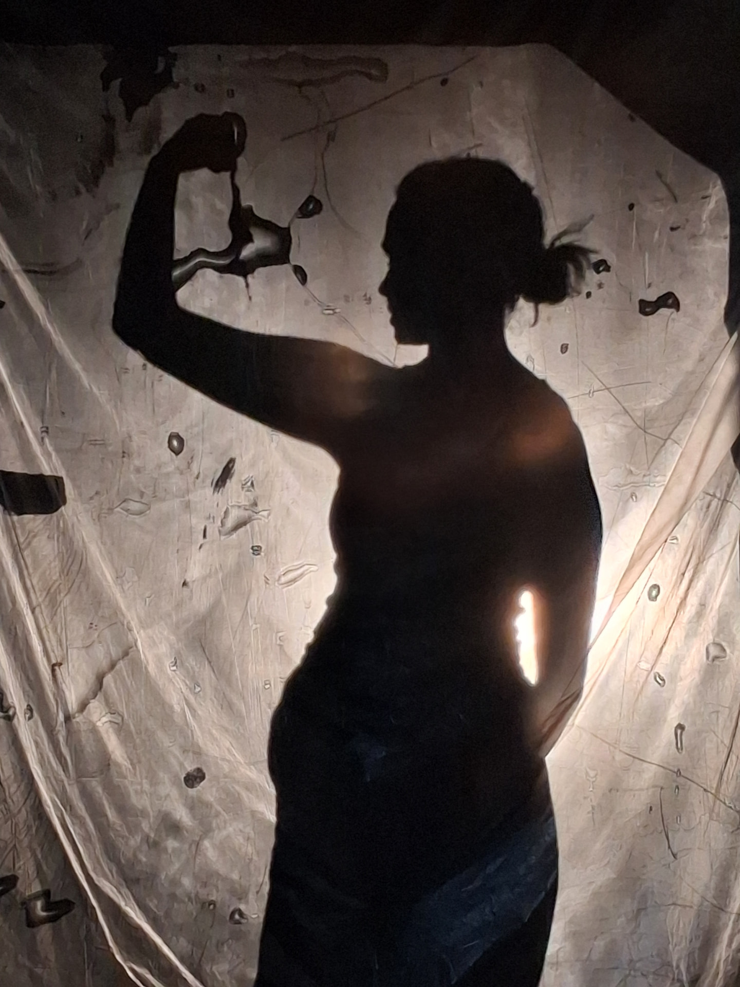 Dark silhouette of a figure behind a translucent wet-paper screen lit amber by the overhead projector, one arm raised