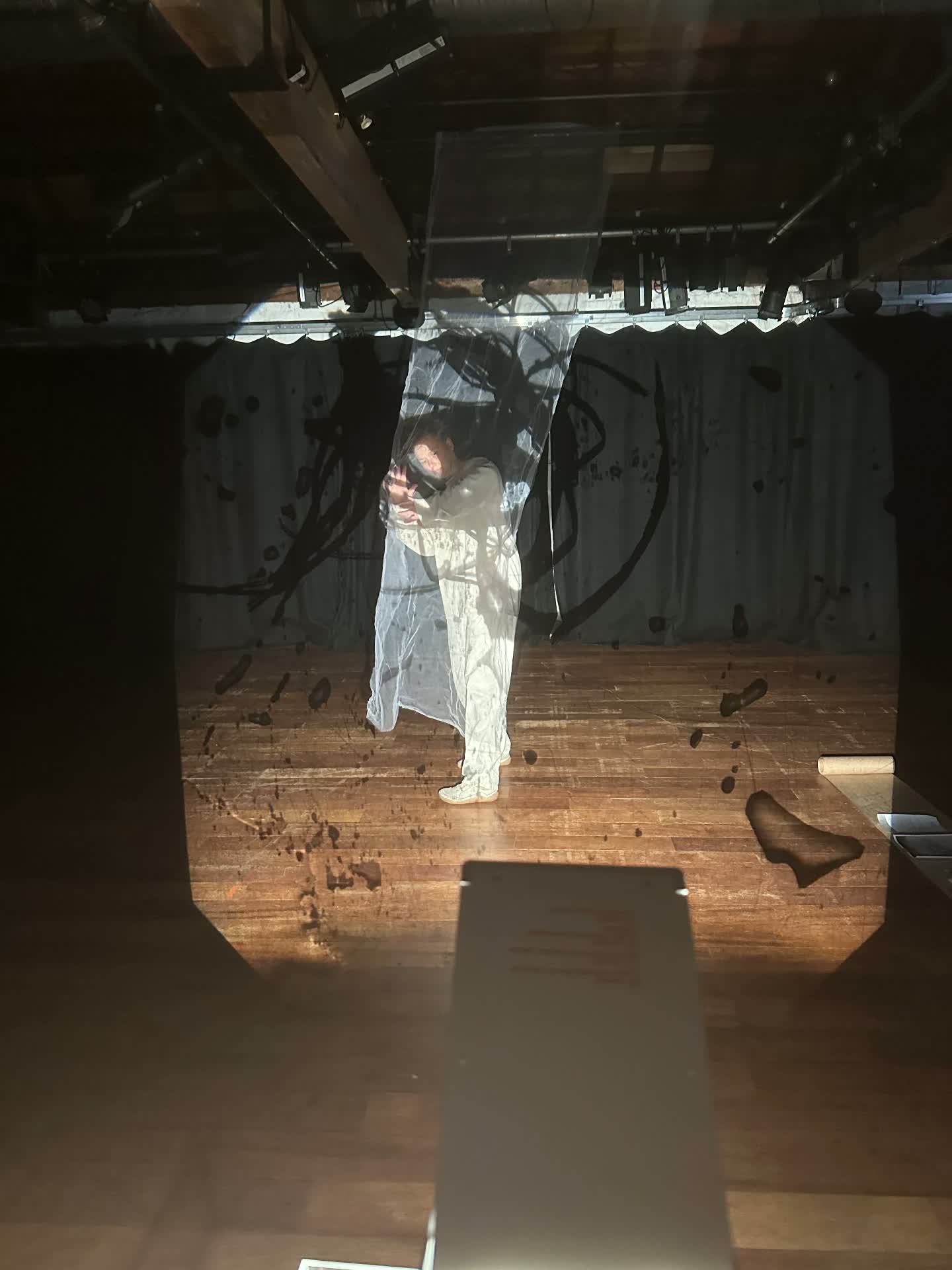 A performer behind hanging gauze with dark ink-like projection washing over body and fabric