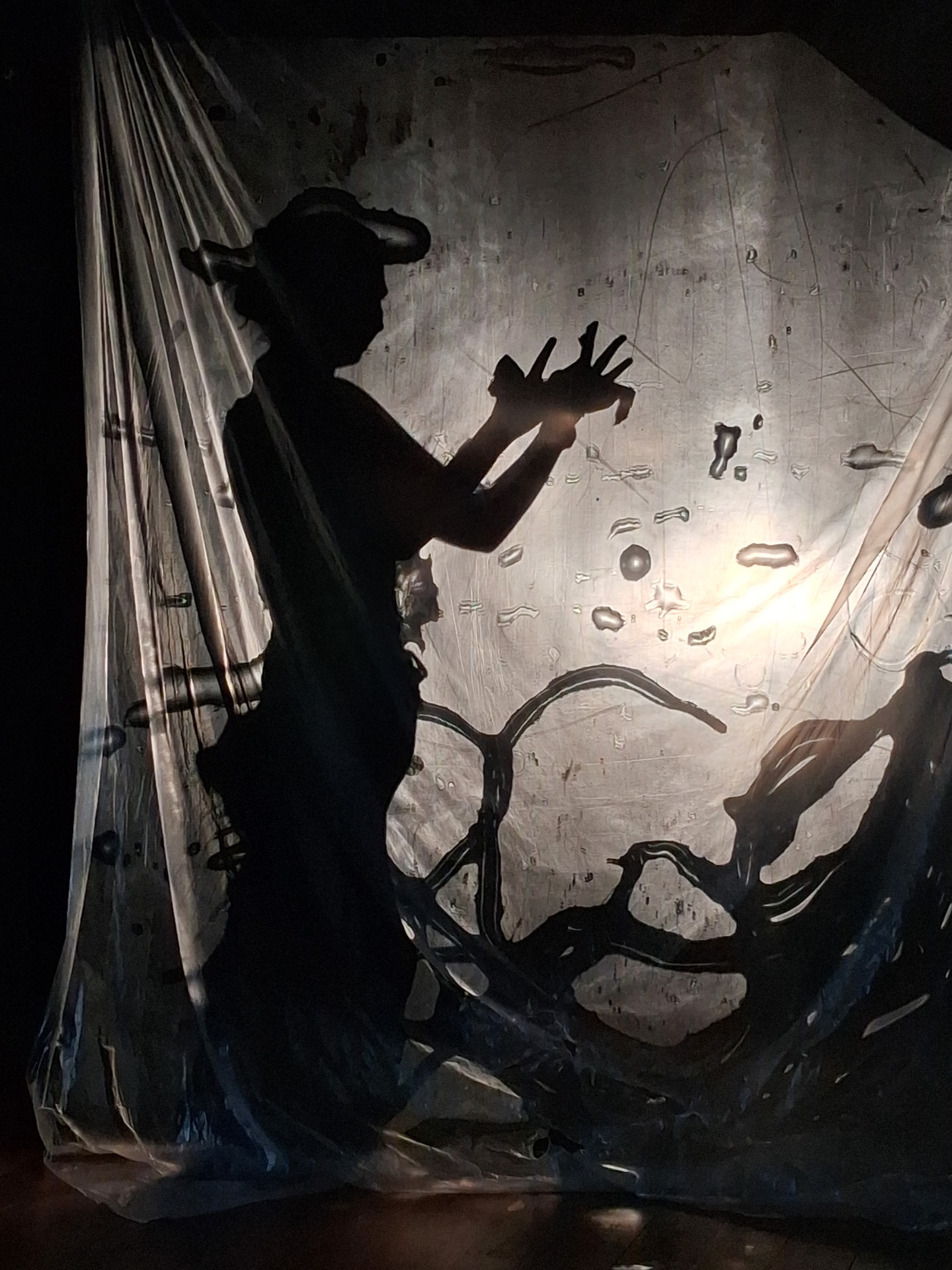 Silhouette of a horned figure behind the textured wet-paper screen, hands splayed near the face